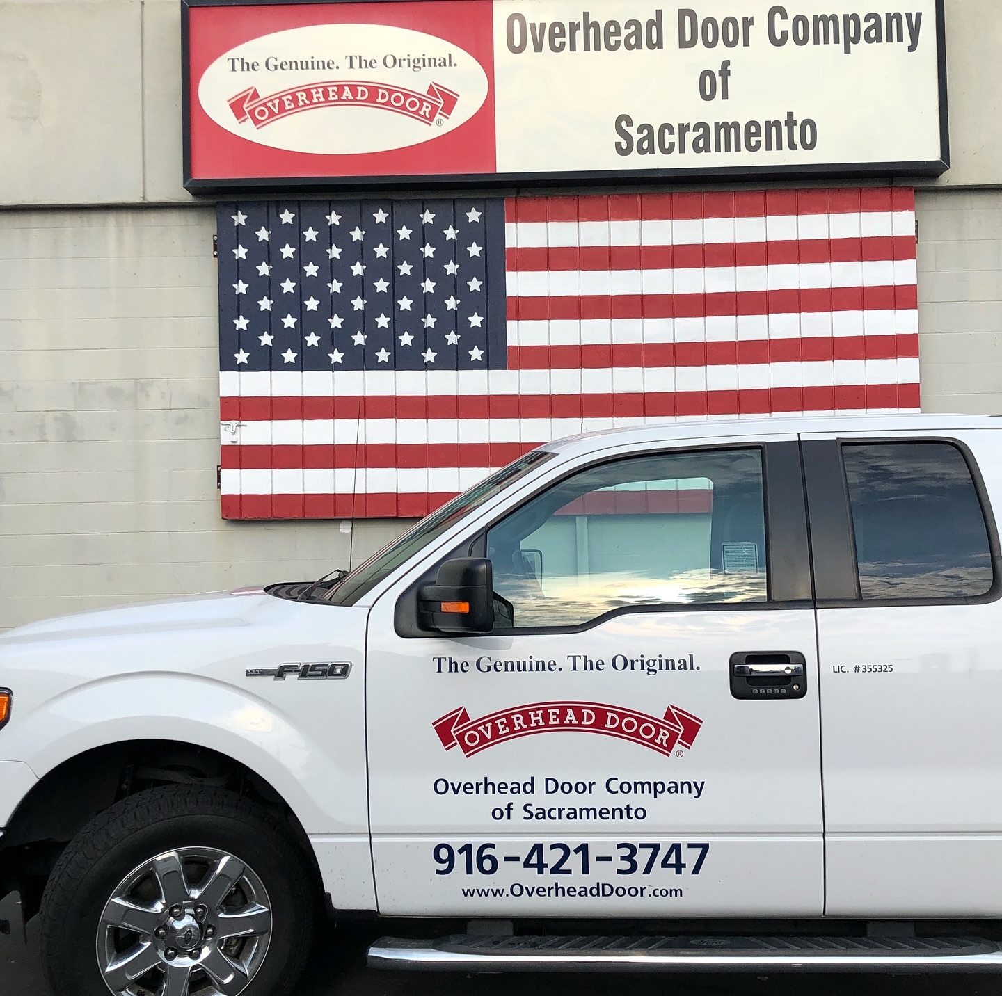 Overhead Door Company of Sacramento truck parked in front of building with American flag backdrop and signage promoting garage door services.