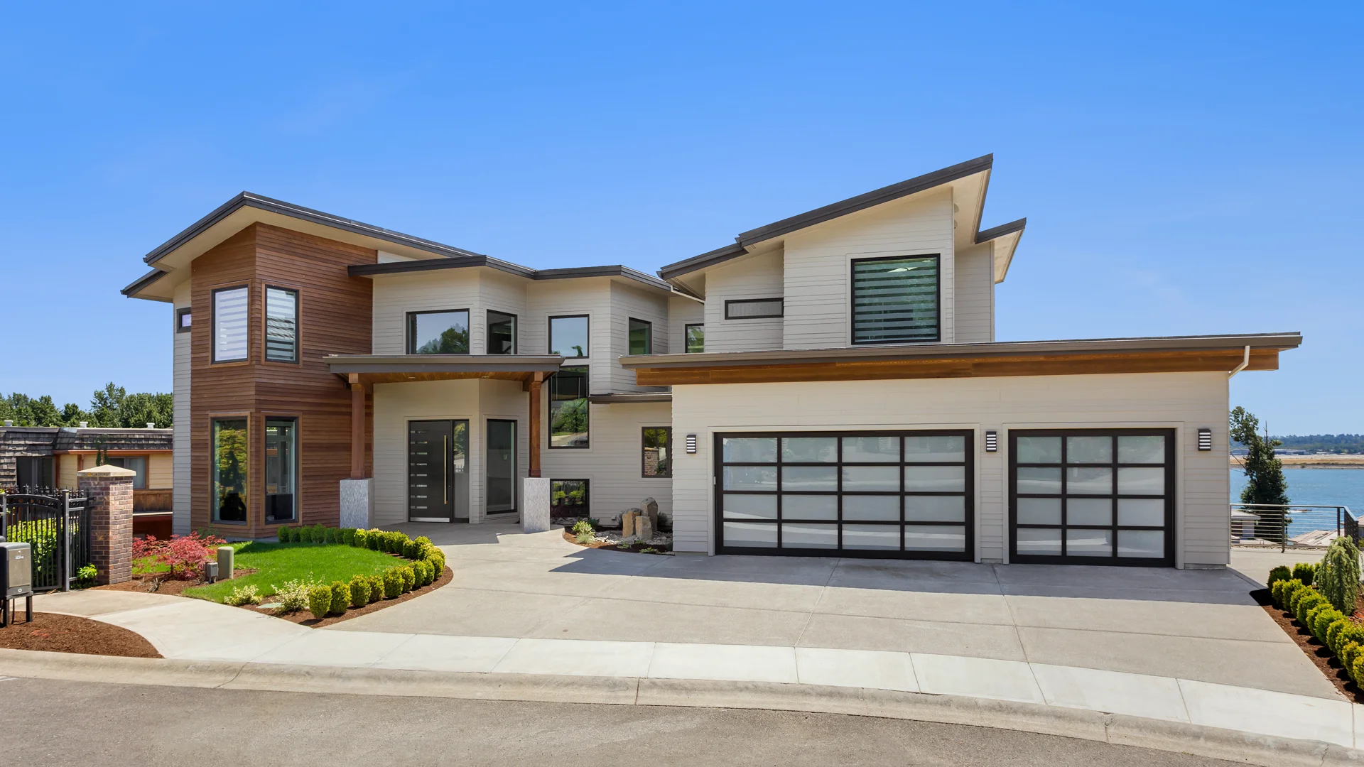 Modern residential home with stylish garage doors, landscaped yard, and clear blue sky, showcasing architectural design and curb appeal.