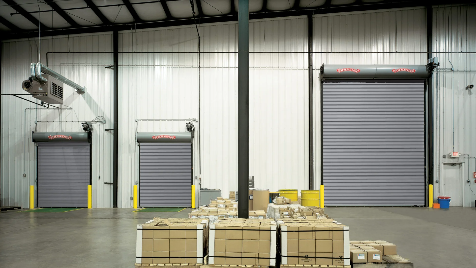 Rolling steel doors in a commercial setting with stacked boxes and industrial features, showcasing Overhead Door™ branding and options for heavy-duty applications.