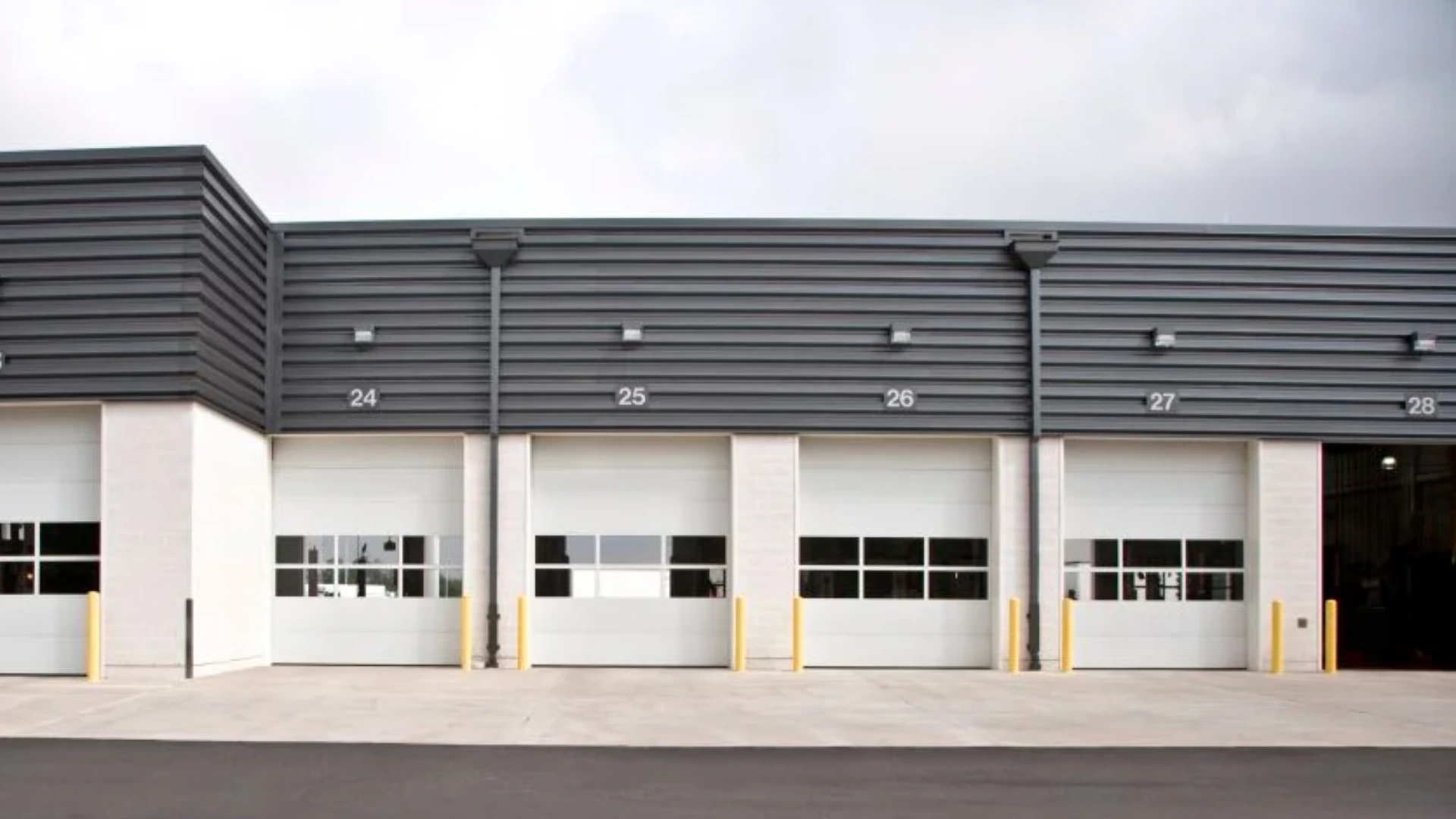 Sectional steel doors in a commercial building, featuring multiple overhead doors with windows, numbered 24 to 28, emphasizing durability and security for industrial use.