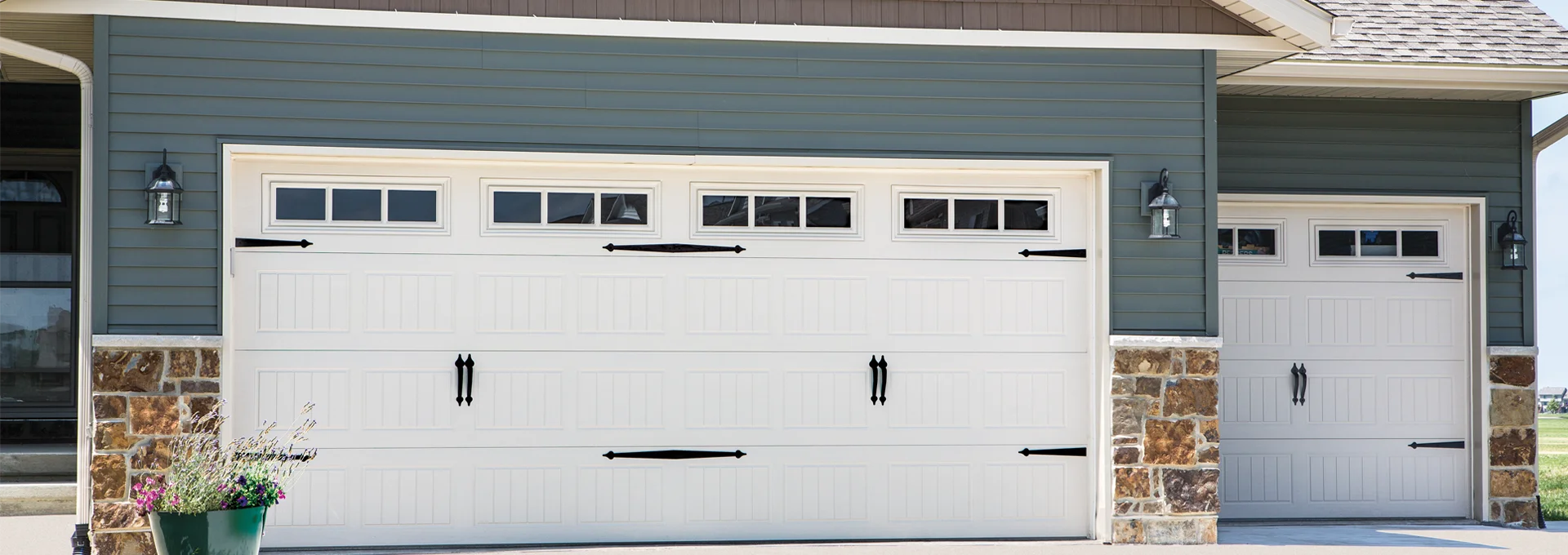 Traditional steel garage door with embossed wood-grain texture, featuring decorative black hardware, installed on a residential home with a stone facade and exterior lighting.