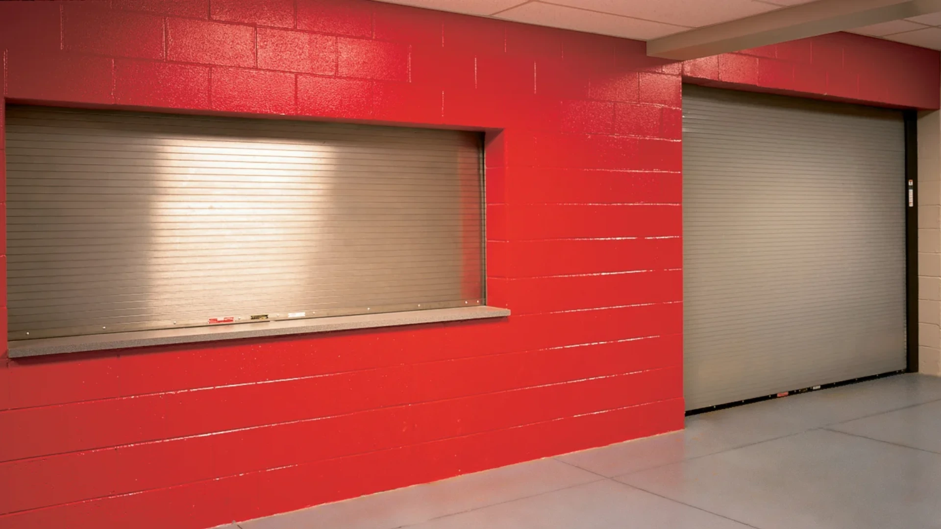 Fire-rated rolling steel door installed in a commercial setting, featuring a red wall and a service window, emphasizing safety and compliance with fire safety standards.