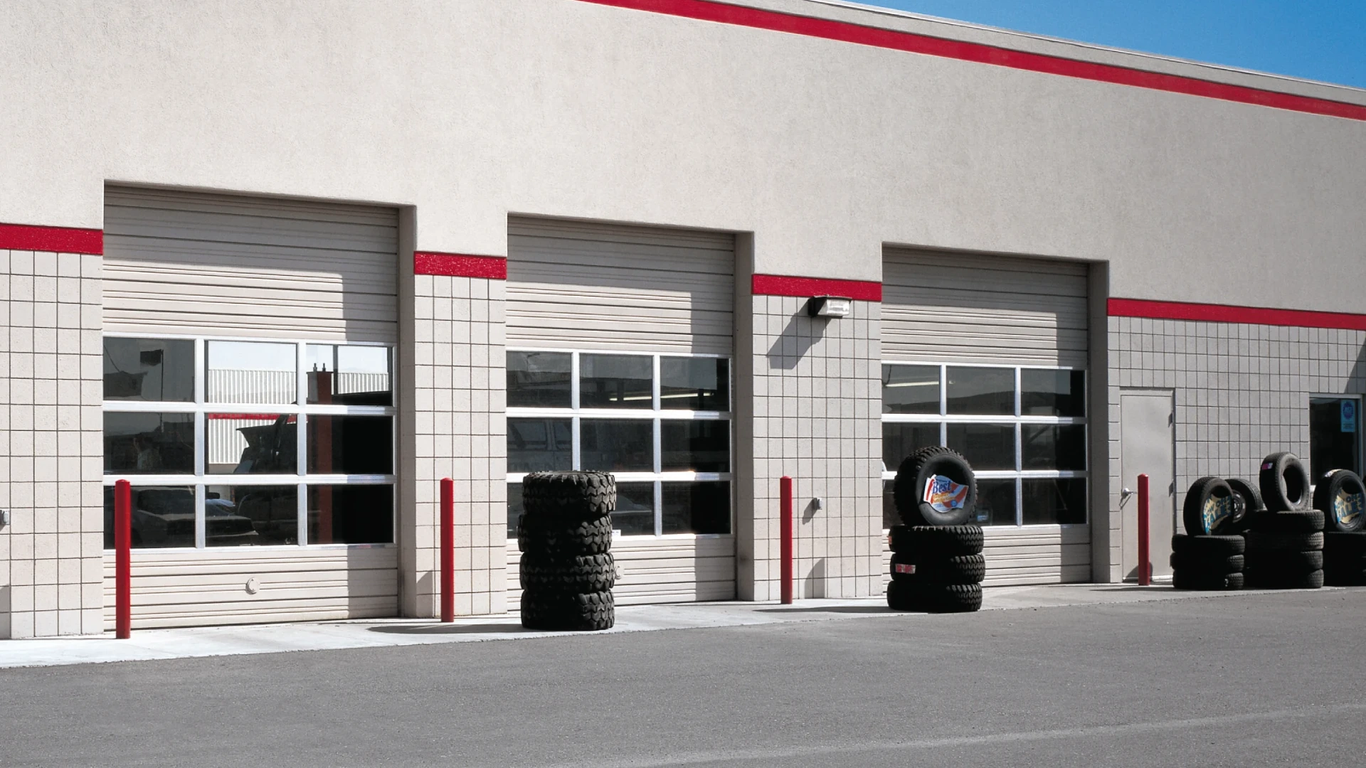 Sectional steel garage doors with glass panels, featuring red accents and surrounded by stacked tires, illustrating commercial overhead door solutions for durability and security.