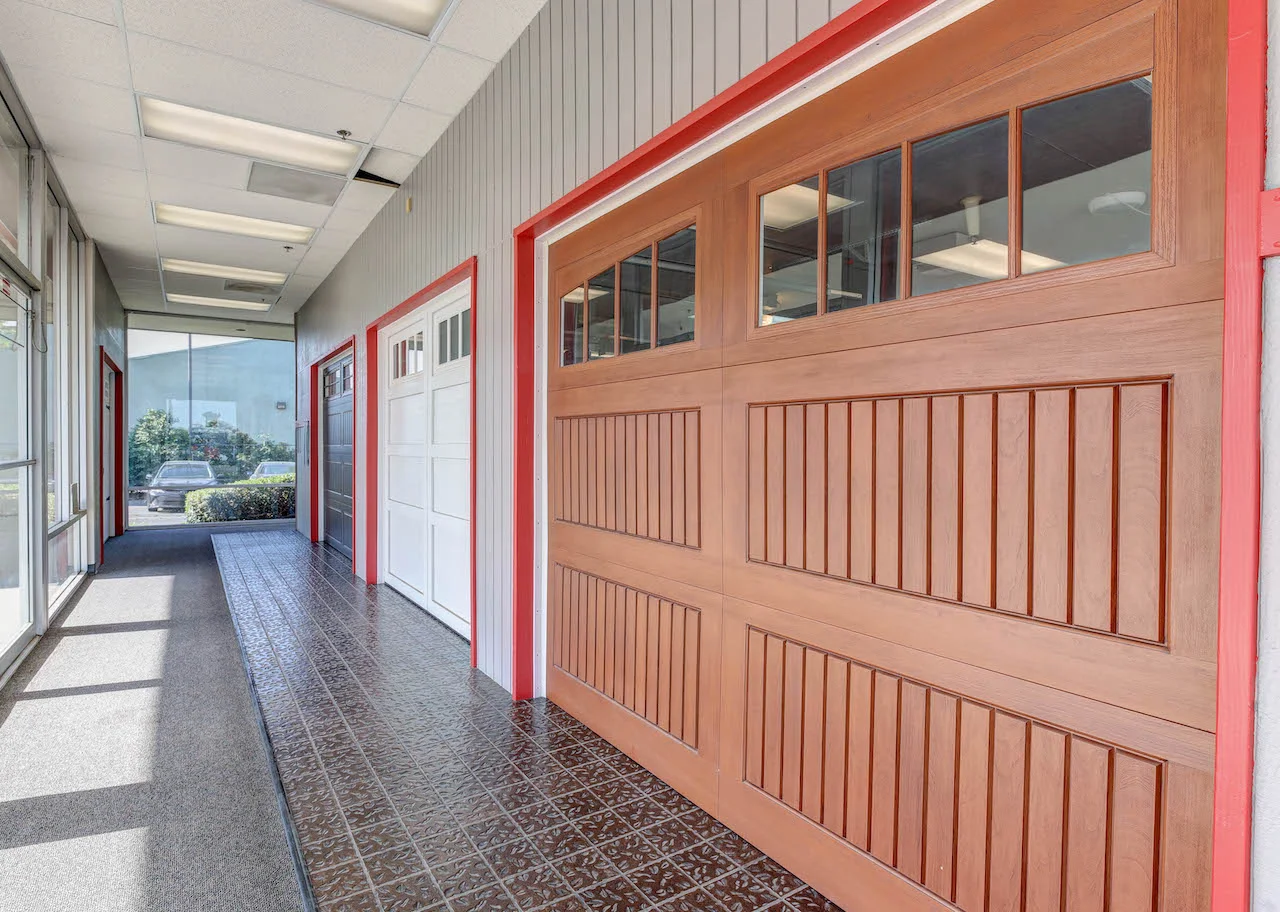 Showroom display of various garage door styles, including a wooden door with windows and two additional garage doors, emphasizing Overhead Door™ products and services in Sacramento.