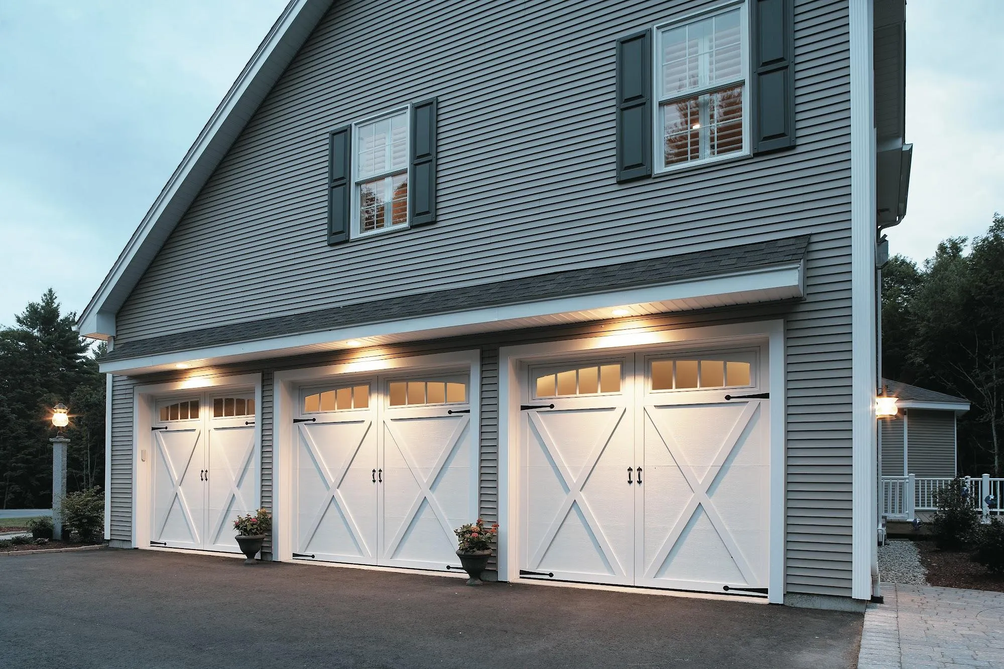 Three white garage doors with decorative windows and outdoor lighting.